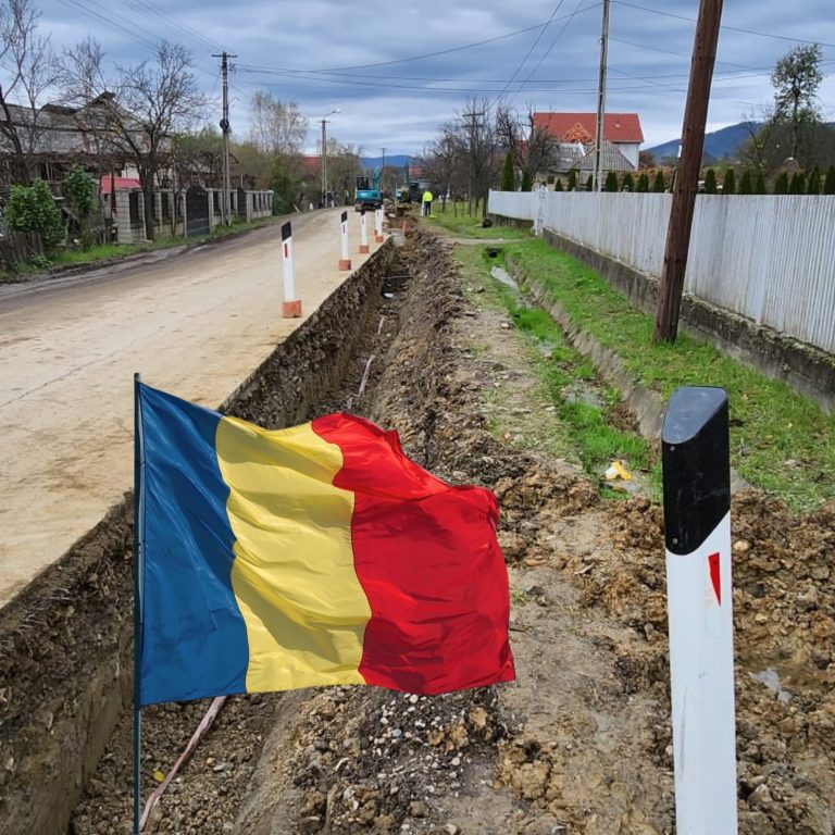 Tranșee pentru rețea de utilități de-a lungul drumului, cu drapelul României